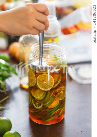 Hand stirring fresh lime slices in a glass jar filled with honey during homemade honey lime infusion preparation. Healthy drink, natural ingredients, and food preservation concept Hand stirring fresh lime slices in a glass jar filled with honey during homemade honey lime infusion preparation. Healthy drink, natural ingredients, and food preservation concept 141206623