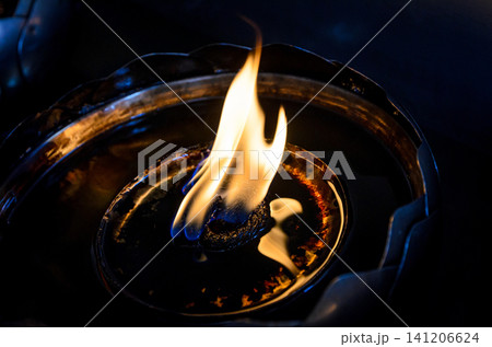 Close-up of a traditional oil lamp with a glowing flame in low light, symbolizing peace, spirituality, meditation, and hope Close-up of a traditional oil lamp with a glowing flame in low light, symbolizing peace, spirituality, meditation, and hope 141206624