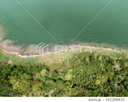 Drone aerial view of a large freshwater lake bordered by lush forest and distant mountains beneath expansive blue skies, showcasing natural landscape and tranquil scenery Drone aerial view of a large freshwater lake bordered by lush forest and distant mountains beneath expansive blue skies, showcasing natural landscape and tranquil scenery 141206632