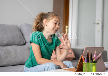 Happy schoolgirl waving during an online class at home Happy schoolgirl waving during an online class at home 141206803
