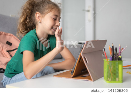 Happy schoolgirl waving during an online class at home Happy schoolgirl waving during an online class at home 141206806