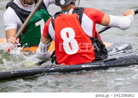Two athletes in colorful jerseys engage in canoe polo on a water surface, one wearing a red jersey with the number eight and the other in green with the number one 141206862