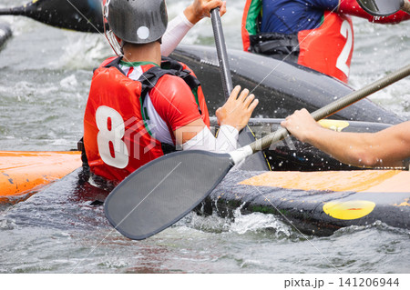 Canoe polo players in colorful jerseys maneuvering their kayaks on a river, with splashes of water and paddles visible in an active sports setting Canoe polo players in colorful jerseys maneuvering their kayaks on a river, with splashes of water and paddles visible in an active sports setting 141206944