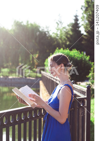 Young woman immersed in book reading. Digital detox by choice. Modern mindfulness practice outdoors on nature. Book lovers day Young woman immersed in book reading. Digital detox by choice. Modern mindfulness practice outdoors on nature. Book lovers day 141207409