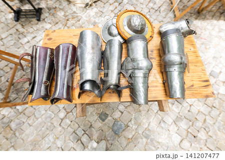 Display of different pieces of armor on a wooden table at a market event in a historical setting 141207477