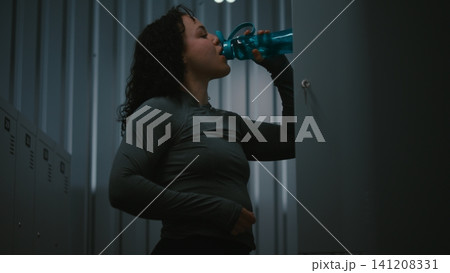 Sporty Female Athlete Getting Ready for Training Session in Dark Dressing Room 141208331