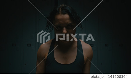 Determined Sportswoman with Intense Glare in Dark Dressing Room Determined Sportswoman with Intense Glare in Dark Dressing Room 141208364