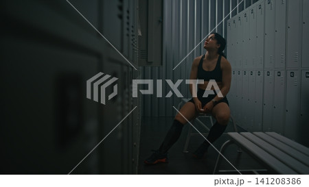Sporty Female Athlete Focusing and Using on Earbuds in Dressing Room Sporty Female Athlete Focusing and Using on Earbuds in Dressing Room 141208386