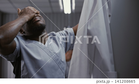 Male Doctor Undressing at Locker, Rubbing Face after Long Hospital Shift Male Doctor Undressing at Locker, Rubbing Face after Long Hospital Shift 141208665