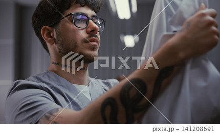Tired Young Doctor in Glasses Removing Face Mask and Rubbing Eyes in Hospital Locker Room 141208691