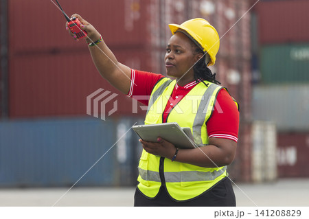 Black foreman woman worker checking stock at container yard, holding laptop computer operate loading containers. Logistics import export shipping concept. Black foreman woman worker checking stock at container yard, holding laptop computer operate loading containers. Logistics import export shipping concept. 141208829