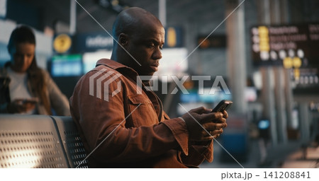 Focused Black Male Passenger Comparing Smartphone Data with Airport Information Board Focused Black Male Passenger Comparing Smartphone Data with Airport Information Board 141208841