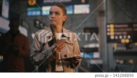 Elegant Woman in Trench Coat Scanning Mobile Ticket and Checking Flight Board Elegant Woman in Trench Coat Scanning Mobile Ticket and Checking Flight Board 141208850