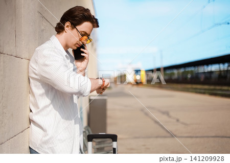 Man checking time on his watch and talking on a smartphone while waiting on a train station platform. A passenger ready for travel. 141209928