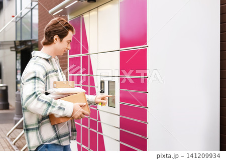 Man using a touch screen at a self-service parcel locker to collect packages, representing an efficient online shopping delivery service. Man using a touch screen at a self-service parcel locker to collect packages, representing an efficient online shopping delivery service. 141209934