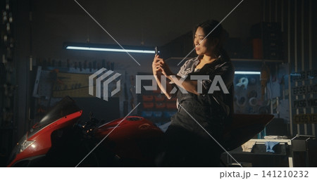 Young Biker Pauses in Modern Garage Checking Message on Smartphone Young Biker Pauses in Modern Garage Checking Message on Smartphone 141210232