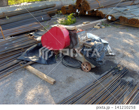 A heavy-duty red industrial rebar bending or cutting machine sits on a concrete site, surrounded by numerous stacks of steel rebar rods. The equipment appears ready for use in a construction projec 141210258