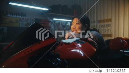 Biker Girl Admiring Sunlight In Sun Drenched Industrial Garage. 141210285