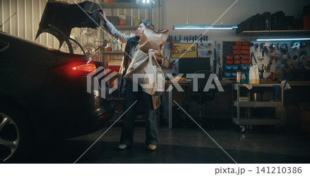 Female in Elegant Trench Coat Unloads Shopping Bags From Car in Garage Female in Elegant Trench Coat Unloads Shopping Bags From Car in Garage 141210386