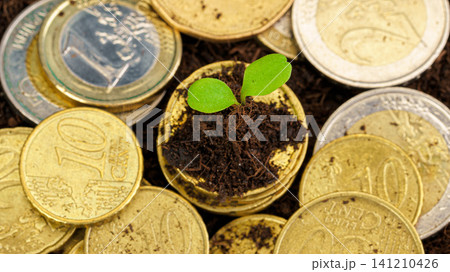 Seedling grows from soil on a pile of coins in a simple indoor setting 141210426
