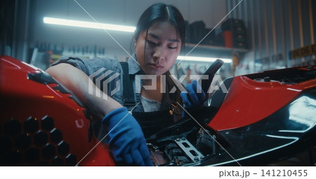 Young Woman Repairing Motorcycle in Modern Garage Uses Smartphone With Voice AI Assistant Young Woman Repairing Motorcycle in Modern Garage Uses Smartphone With Voice AI Assistant 141210455