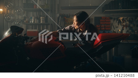 Female Rider in Workwear Carefully Polishes Her Sport bike in Warm Sunlight Female Rider in Workwear Carefully Polishes Her Sport bike in Warm Sunlight 141210488