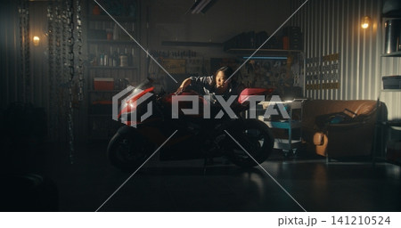 Woman Lovingly Clean Motorcycle in Modern Garage Filled With Golden Light Woman Lovingly Clean Motorcycle in Modern Garage Filled With Golden Light 141210524