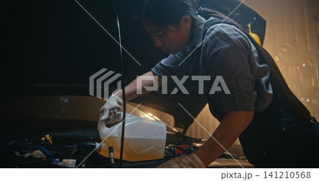 Professional Woman Auto Technician Refills Automotive Fluid Under Hood in Modern Workshop Professional Woman Auto Technician Refills Automotive Fluid Under Hood in Modern Workshop 141210568