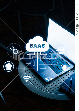 Saas software icon over laptop and notes on round table in office setting at night 141210587