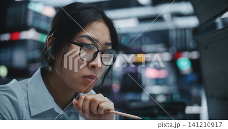 Highly Focused Female Trader Analyzing Extensive Market Data With Pencil in Hand Highly Focused Female Trader Analyzing Extensive Market Data With Pencil in Hand 141210917