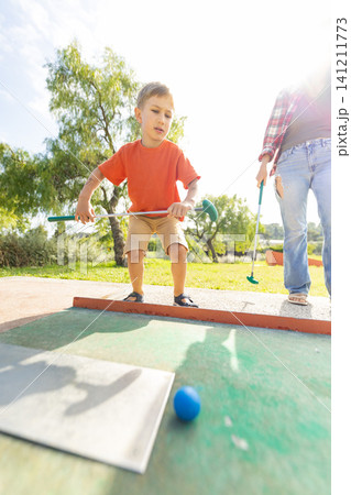 Boy plays mini golf with adult in sunny outdoor park during a fun afternoon activity together Boy plays mini golf with adult in sunny outdoor park during a fun afternoon activity together 141211773