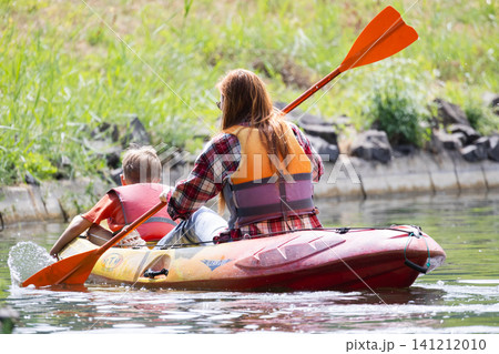 Family enjoys time kayaking on a sunny day near a calm waterside area surrounded by greenery 141212010