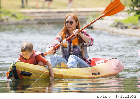 Mother and son paddle a kayak on a calm pond during a sunny afternoon in a park setting Mother and son paddle a kayak on a calm pond during a sunny afternoon in a park setting 141212052