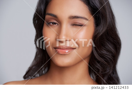 Woman, face and wink with beauty and skincare glow, playful and fun with lip gloss for moisturizer on grey background. Flirt in portrait, natural cosmetics and hair care with wellness and dermatology Woman, face and wink with beauty and skincare glow, playful and fun with lip gloss for moisturizer on grey background. Flirt in portrait, natural cosmetics and hair care with wellness and dermatology 141212433