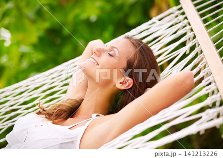 Happy woman, rest and wellness on hammock in outdoor, peace and summer vacation in sunshine in nature. Young person, smile and sleep by trees at beach resort, calm and holiday for leisure on island 141213226
