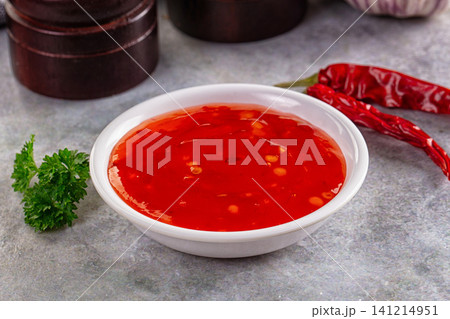 Vibrant red chili sauce in white bowl with dried peppers and parsley on gray surface Vibrant red chili sauce in white bowl with dried peppers and parsley on gray surface 141214951