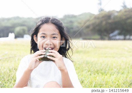 おにぎりを美味しそうに食べる小学生の女の子 141215649