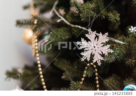 Glittering snowflake ornament on a decorated Christmas tree with festive lights and golden garland. Cozy winter holiday background for Christmas, New Year, celebration, seasonal greeting, and festive Glittering snowflake ornament on a decorated Christmas tree with festive lights and golden garland. Cozy winter holiday background for Christmas, New Year, celebration, seasonal greeting, and festive 141215885