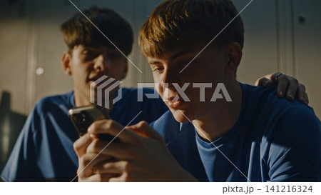 Teenage Footballers Looking at Smartphone and Talking in Locker Room Teenage Footballers Looking at Smartphone and Talking in Locker Room 141216324