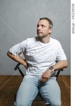 Casual studio portrait of a middle aged man sitting in a chair Casual studio portrait of a middle aged man sitting in a chair 141216530