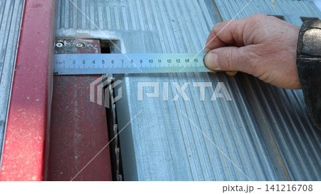 the hand of a craftsman using a metal ruler to measure the distance from the rip fence to the saw blade on a circular saw for precise adjustment before making a cut. the hand of a craftsman using a metal ruler to measure the distance from the rip fence to the saw blade on a circular saw for precise adjustment before making a cut. 141216708