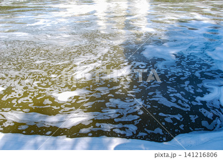 White foam floating on murky river water surface. 141216806