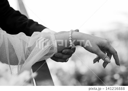 Groom holding bride hand with pearl bracelet and lace sleeve in monochrome wedding photography. Groom holding bride hand with pearl bracelet and lace sleeve in monochrome wedding photography. 141216888