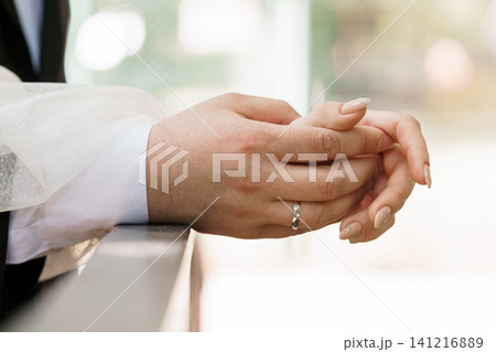 Close up of couple holding hands with wedding ring on finger during marriage ceremony in bright white light. 141216889