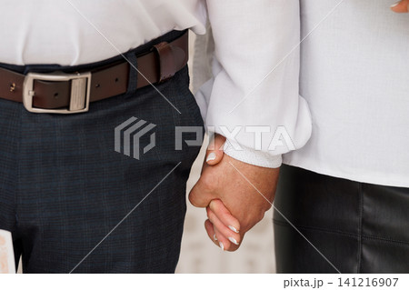 Close up of a man and woman holding hands wearing formal white shirts and dark trousers and skirt. 141216907