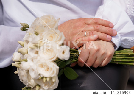 Close up of groom hands holding bridal bouquet of white roses with wedding ring on finger Close up of groom hands holding bridal bouquet of white roses with wedding ring on finger 141216908