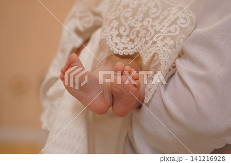 Close up of newborn baby feet in white lace christening gown against a soft neutral background. Close up of newborn baby feet in white lace christening gown against a soft neutral background. 141216928