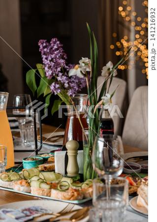 Elegant table setting with purple lilacs and appetizers for a celebratory dinner party in a cozy interior. 141216932