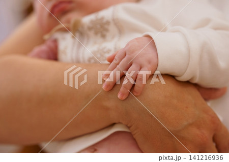 Newborn baby hand resting on adult arm in soft white clothing with warm natural lighting. Newborn baby hand resting on adult arm in soft white clothing with warm natural lighting. 141216936