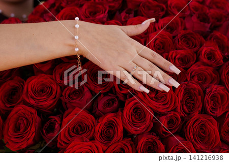Elegant female hand with pearl bracelet and gold ring resting on a bed of deep red roses. Elegant female hand with pearl bracelet and gold ring resting on a bed of deep red roses. 141216938